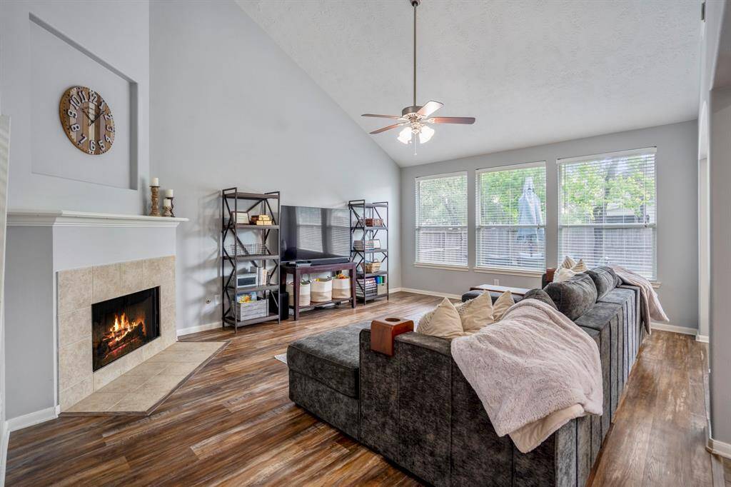 The spacious living room boasts a two-story vaulted ceiling, creating an open and airy feel. A corner fireplace with a trimmed mantle and a recessed art niche above add a touch of elegance. Large windows offer a serene view of the backyard, flooding the space with natural light.