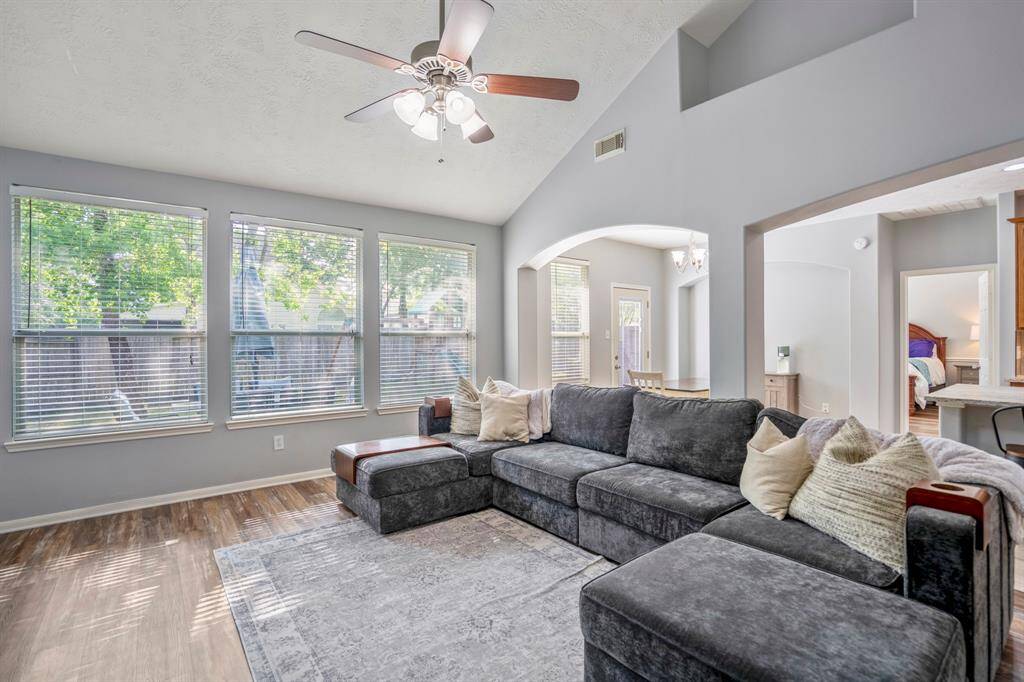 From near the fireplace, this view captures the backyard through large windows that fill the space with natural light. Just off the kitchen, a glimpse into the downstairs primary bedroom highlights the home’s thoughtful layout.