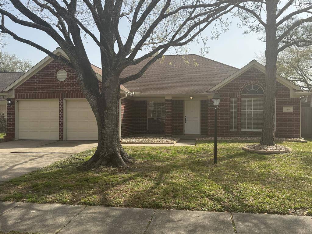 Charming brick home with a gabled roof and a two-car garage. It features a front porch, large arched window, and mature trees in the yard, creating a welcoming and cozy atmosphere.