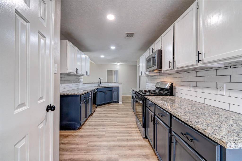 Modern kitchen with granite countertops, stainless steel appliances, and a mix of upper white and lower dark cabinets. The space features laminate wood flooring and subway tile backsplash, offering a sleek, contemporary look.