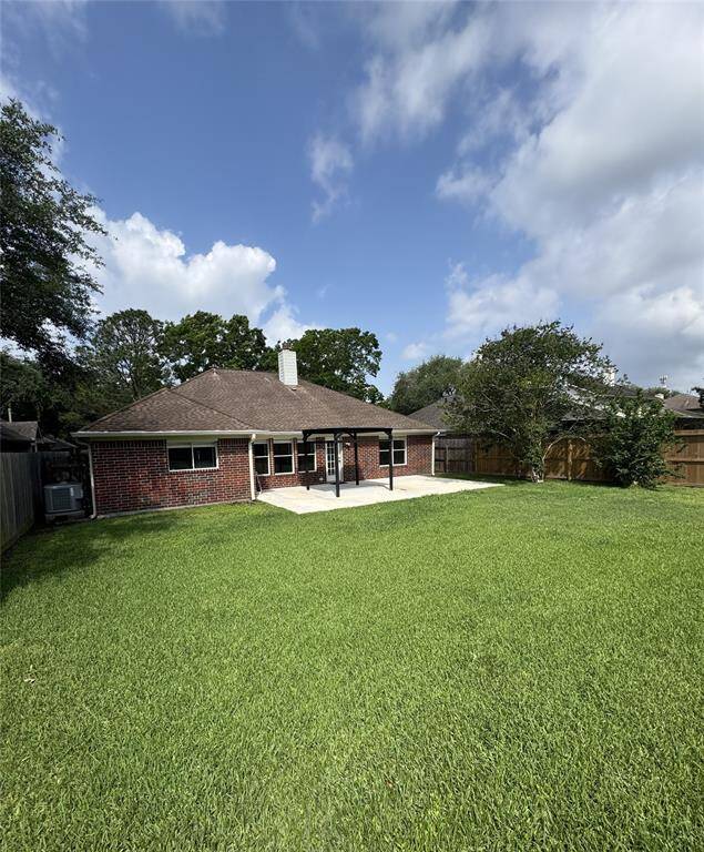 This photo shows a single-story brick house with a spacious, well-maintained backyard. There's a small patio area, ideal for outdoor gatherings, and the yard is enclosed by wooden fencing, offering privacy.