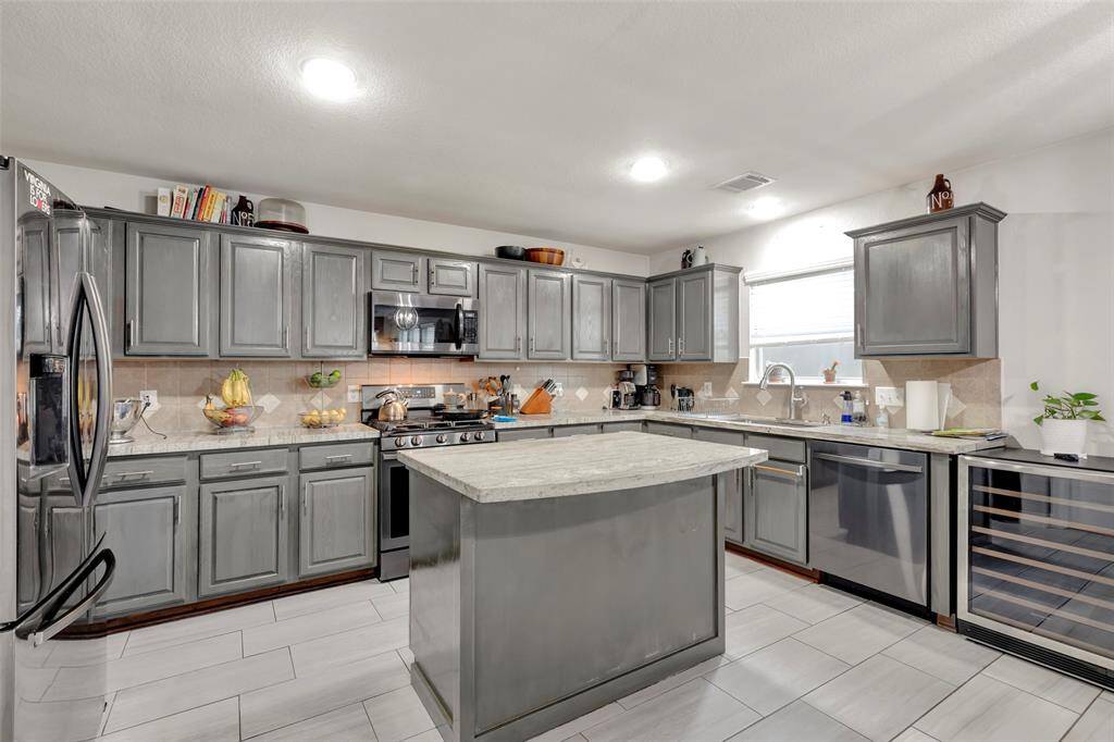 Spacious kitchen with a central island, stainless steel appliances, and stylish sage gray cabinets.