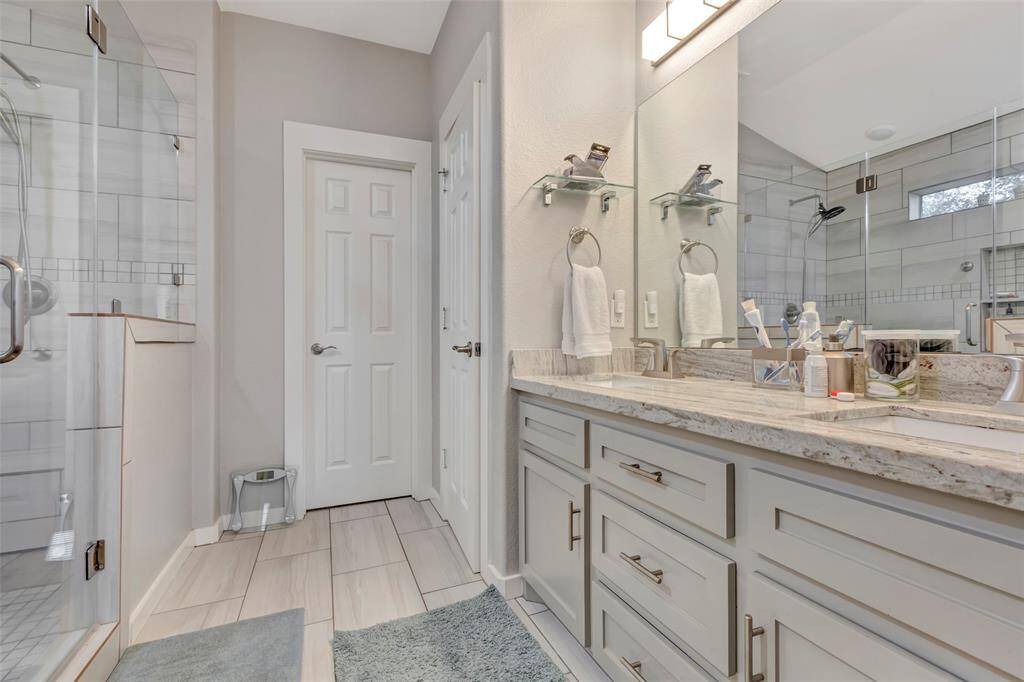 The primary bathroom boasts double sinks, granite countertops, a glass-enclosed shower, and tiled flooring.