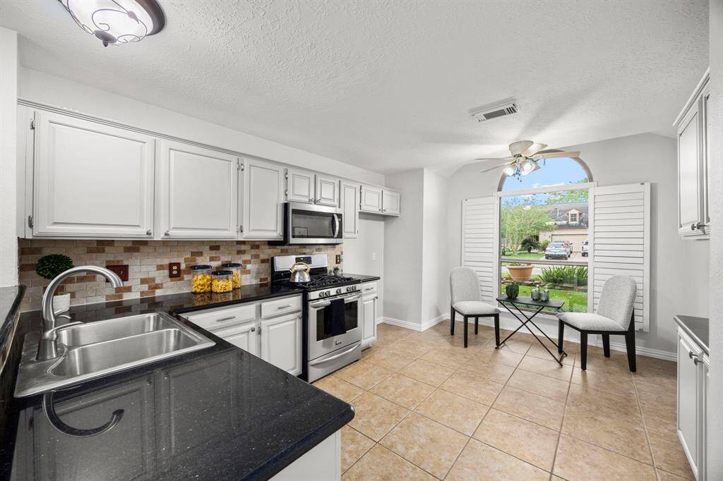 This kitchen features modern appliances, freshly painted cabinetry, and a sleek black granite countertop. The space is brightened by a large window with shutters, offering a view of the outdoors.