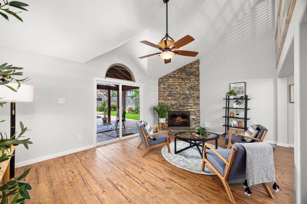 Bright and inviting living room with vaulted ceilings, featuring a stone fireplace and wood look tile floors. Sliding doors lead to a patio, offering a seamless indoor-outdoor flow.
