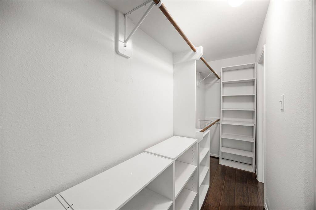 Spacious walk-in primary closet with built-in shelving and hanging rods, featuring wood look floors and bright lighting. Ideal for organized storage and easy access.