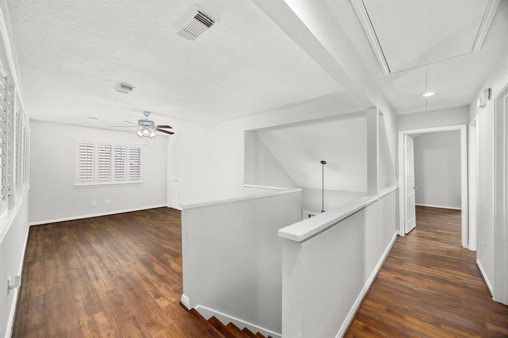 This photo showcases a bright, open upstairs hallway with warm luxury vinyl plank flooring  and ample natural light from the window with shutters. The space connects to multiple rooms, offering a versatile layout.