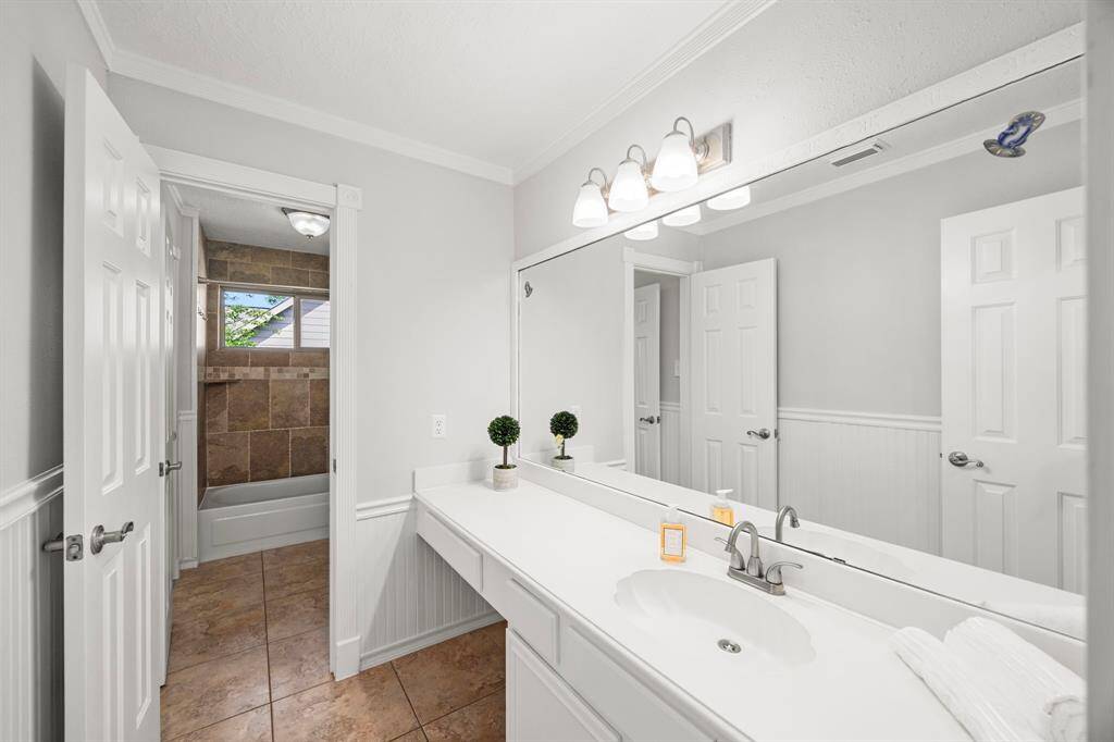 This bathroom features a clean, modern design with a large mirror, ample countertop space, and soft lighting. It includes a shower-tub combo with stylish tile work, and has neutral tones that create a bright, welcoming atmosphere. The toilet/shower area connect to the 4th bedroom.