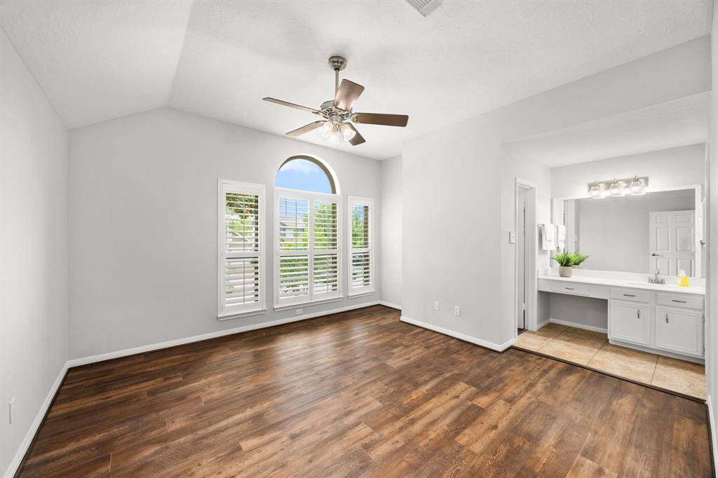 Bedroom 4 is bright & airy featuring a vaulted ceiling with a ceiling fan, luxury vinyl plank flooring, and large arched windows with plantation shutters. This room offers it's own vanity that connects to the shower/toilet area of the hall bath and a large walk-in closet.