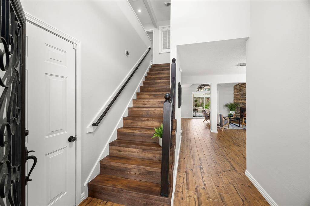 This photo showcases a bright, welcoming entryway with wooden stairs and flooring, leading into a cozy living area with a stone fireplace. The space is modern and inviting, perfect for family gatherings.