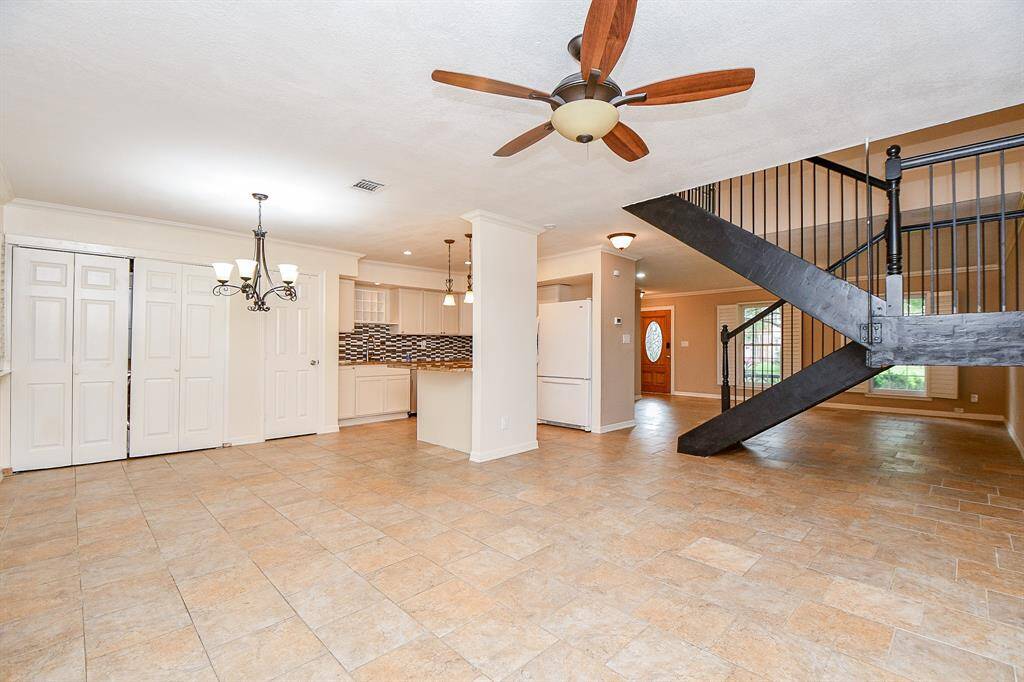 This spacious open-plan area features tiled flooring, a modern ceiling fan, and a striking black staircase. The kitchen includes a stylish backsplash and ample cabinetry, while the adjacent dining area is enhanced by elegant lighting. Suitable for comfortable living and entertaining.