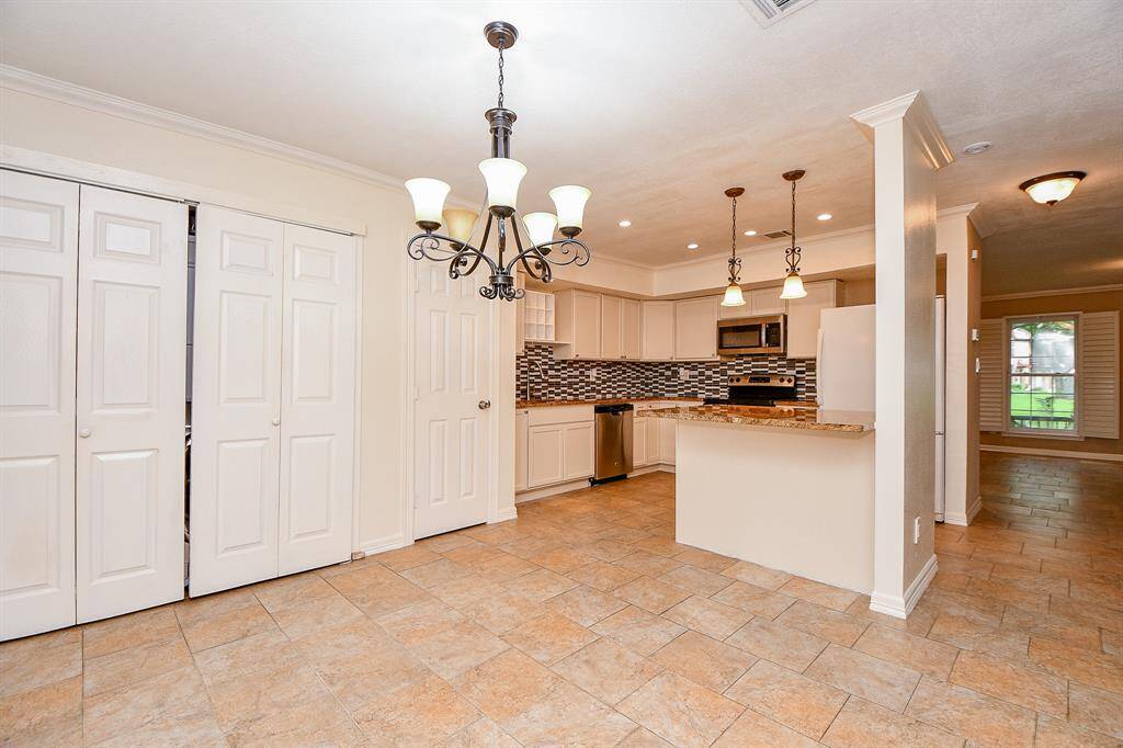 This photo showcases a modern kitchen with a large, open layout. It features tiled flooring, a stylish backsplash, granite countertops, and stainless steel appliances. The room is well-lit with elegant pendant and chandelier lighting. A set of double doors provides additional storage space.