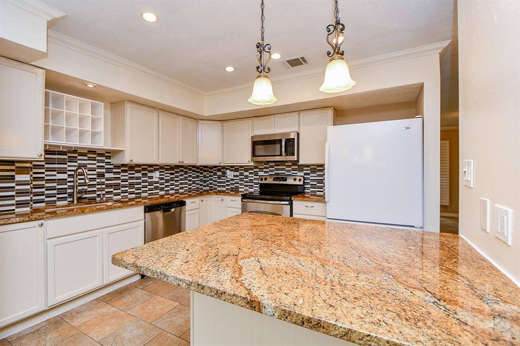 Modern kitchen with granite countertops, stainless steel appliances, and a stylish tile backsplash. Bright lighting and ample cabinetry offer a functional and inviting cooking space.