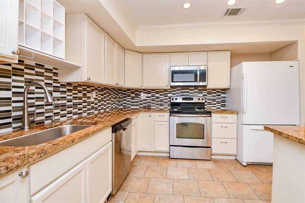 This kitchen features modern appliances with stainless steel finishes, ample cabinetry, and granite countertops. The stylish tiled backsplash and spacious layout make it both functional and inviting.