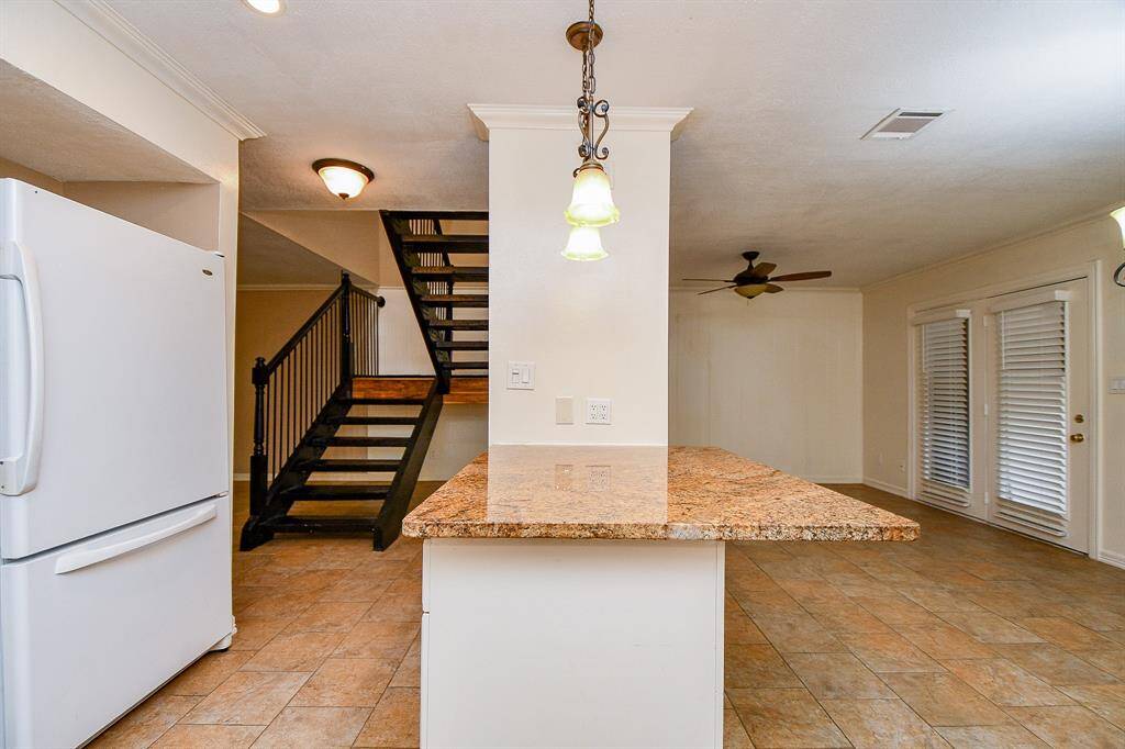 This home features an open-concept layout with a spacious kitchen island, granite countertops, and tile flooring. It includes a modern staircase with metal railings, ceiling fans, and ample natural light from patio doors with shutters. Perfect for contemporary living.