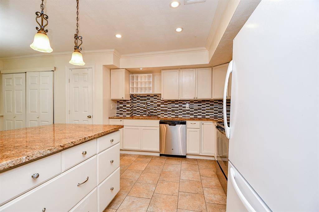 Bright kitchen with modern features, including a large island with granite countertops, stainless steel appliances, tiled backsplash, and ample cabinet storage. Ideal for cooking and entertaining.