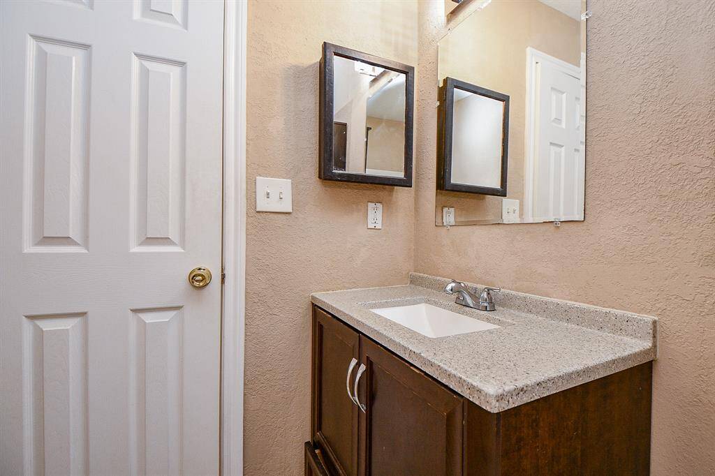 This bathroom features a compact vanity with a granite countertop, under-mount sink, and a wall-mounted mirror cabinet for storage. The neutral walls and white door create a clean, simple look.