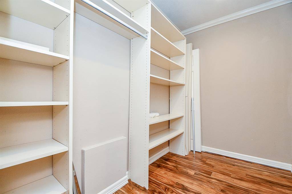 This photo shows a spacious walk-in closet with built-in white shelving, ideal for organized storage. It features warm hardwood flooring and neutral walls, offering a clean and inviting space.