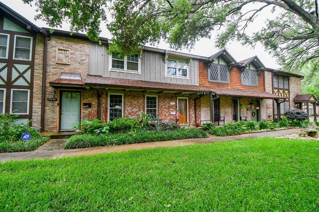 This charming townhouse features a classic brick exterior with Tudor-style accents, nestled in a lush, green setting. It boasts a welcoming front porch, large windows, and mature trees, providing a peaceful ambiance. Ideal for buyers seeking character and natural surroundings.