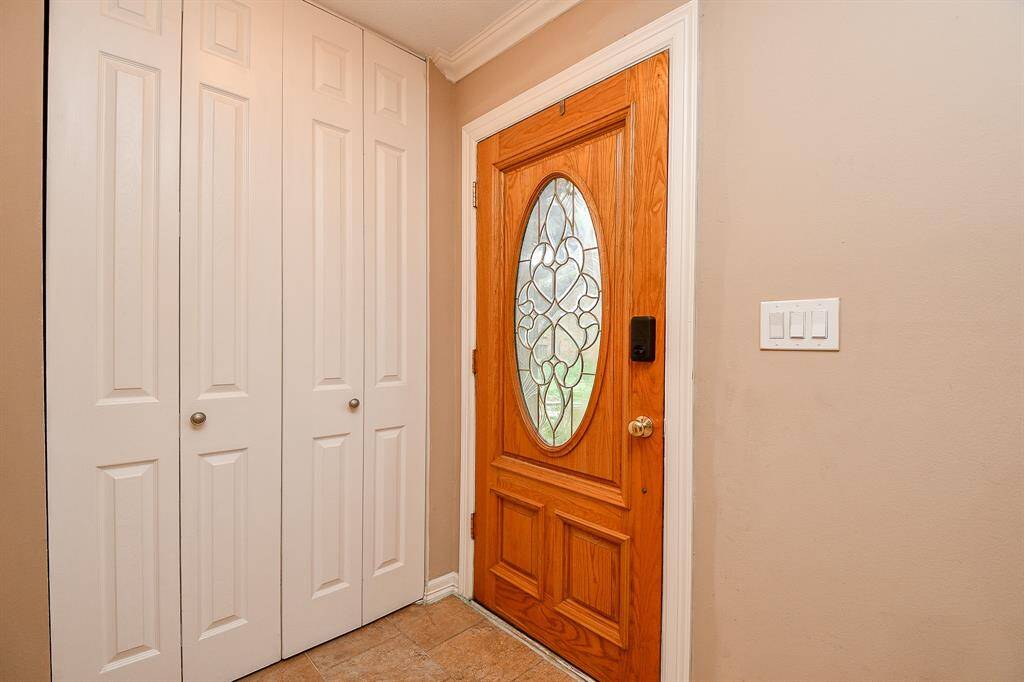 Welcoming entryway with a warm wood front door featuring an oval decorative glass insert. Adjacent are white double-door closets, offering ample storage. Neutral walls and tile flooring complete the inviting space.