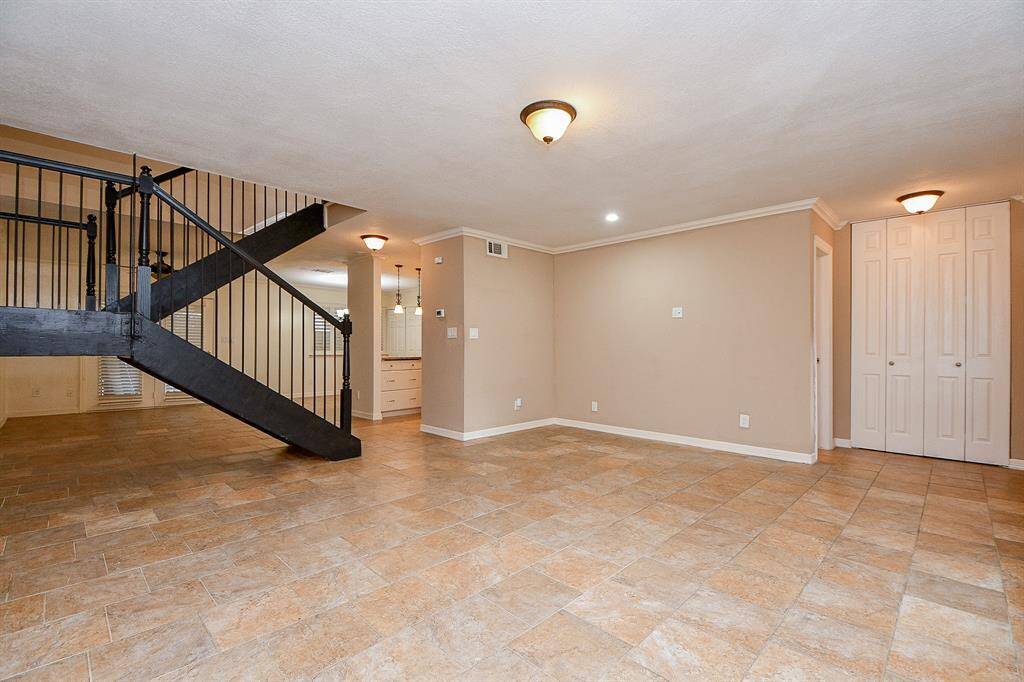 This spacious room features tile flooring, neutral walls, and ample lighting. It includes an elegant black staircase and a closet with double doors, perfect for a versatile living space.