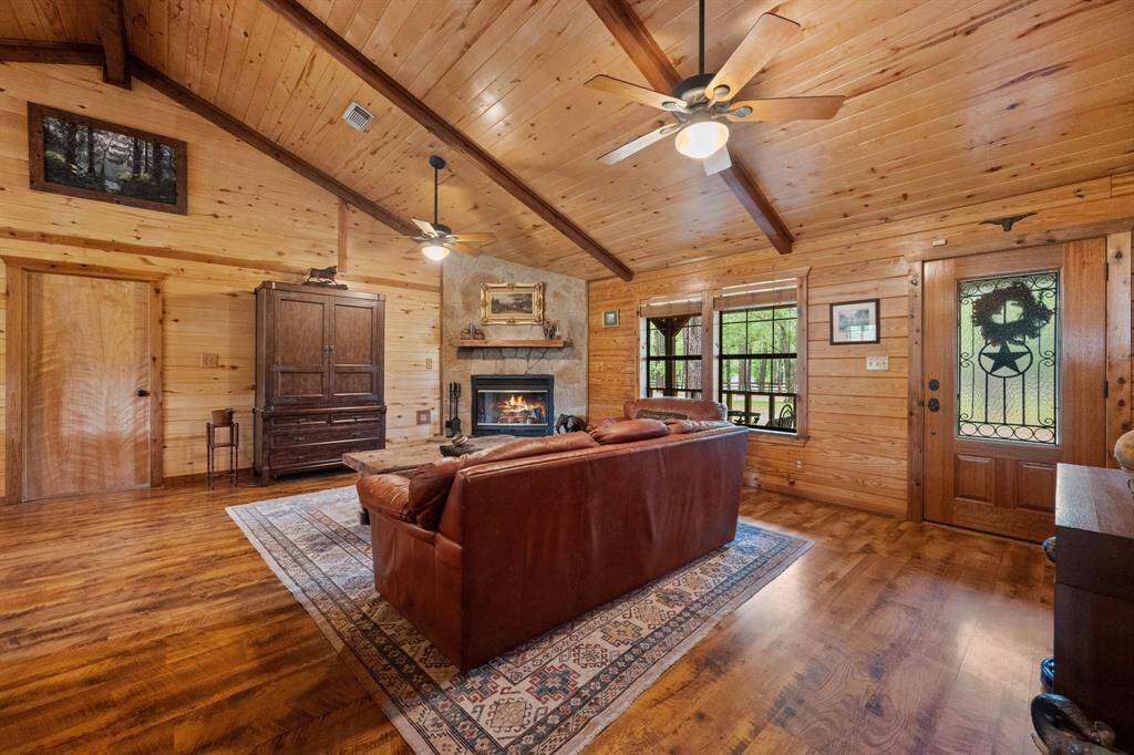 This cozy living room features warm wood paneling, a vaulted ceiling with exposed beams, and a stone fireplace, creating a rustic yet inviting atmosphere.