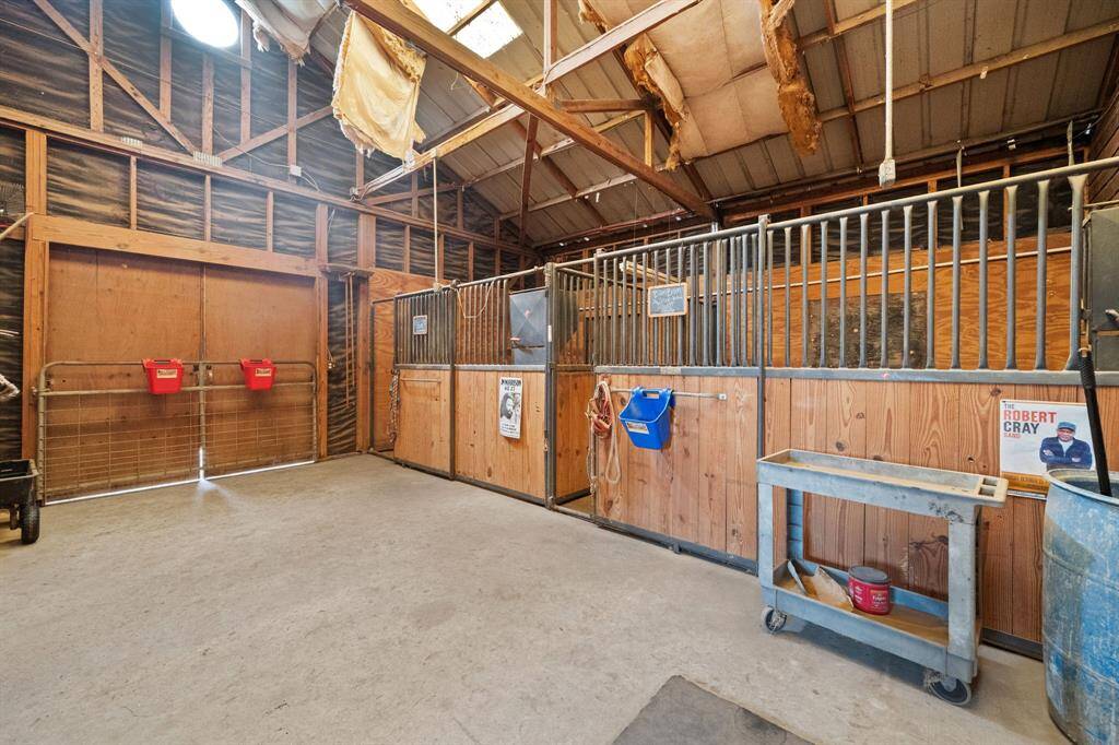 A well-lit horse stable with wooden stalls, metal railings, and storage for equipment, offering functionality for equestrian needs.