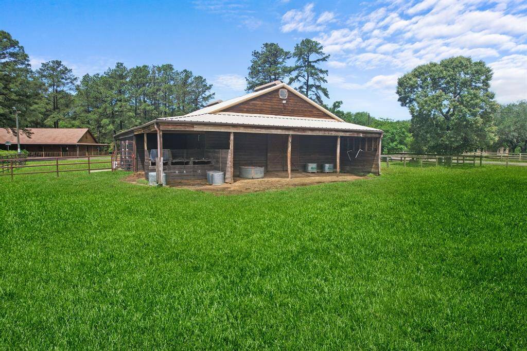 Back view of the barn set on lush green grounds, surrounded by trees and fencing, ideal for equestrian or farming activities.