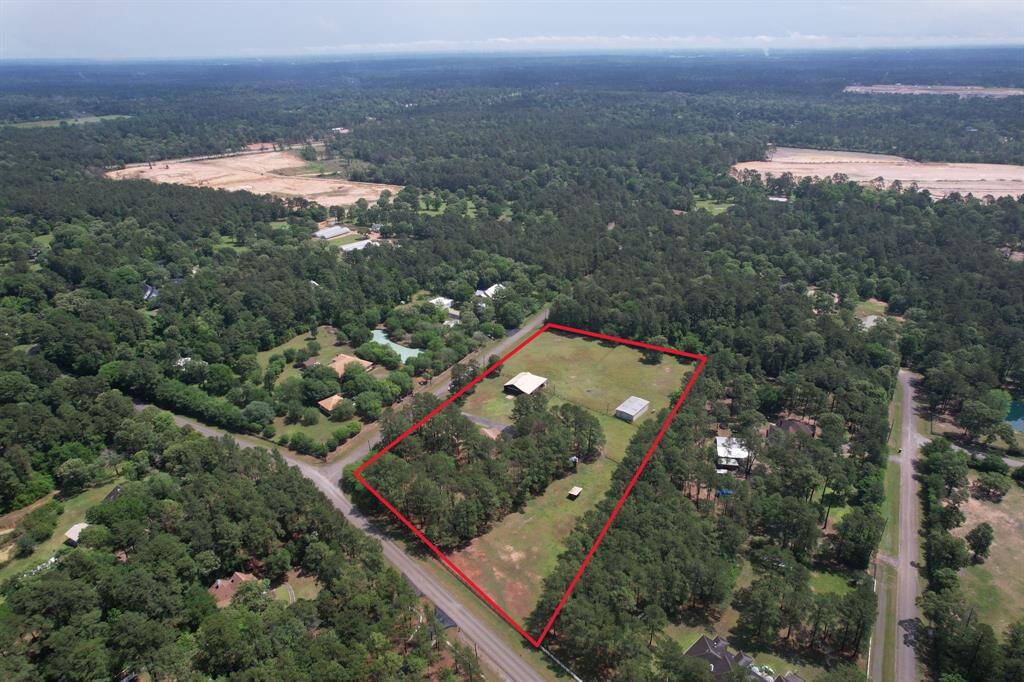 This aerial photo showcases a spacious, tree-lined property outlined in red, featuring open green areas and a few structures. It's situated in a serene, forested setting with nearby roads providing accessibility. Ideal for those seeking privacy and a connection with nature.