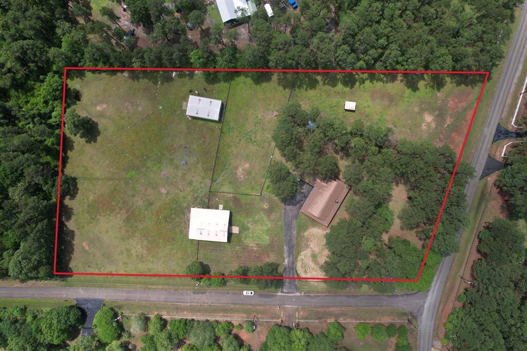 This aerial photo shows a spacious property outlined in red, featuring open green areas, a house, and additional buildings. It's bordered by trees and has road access on two sides, offering both privacy and convenience.