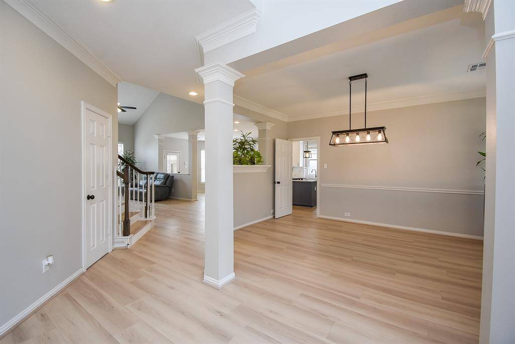 This photo showcases a bright and spacious open-concept living area with light flooring, modern lighting, and neutral wall colors. It features a stylish chandelier and leads to a cozy living room and kitchen area, offering a welcoming and versatile space.
