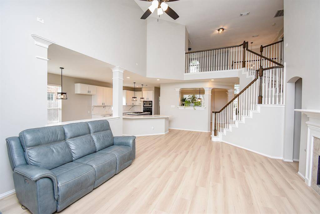 This beautiful home features an open living area with high ceilings, a modern kitchen with white cabinetry, and a cozy seating area. The elegant staircase leads to an upper level, adding to the spacious and airy feel. Perfect for comfortable family living.