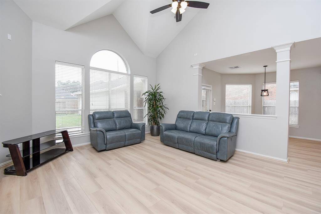 Spacious living room with high ceilings and large windows, allowing plenty of natural light. Adjacent to the breakfast area with a view of the outdoors, creating an open and airy feel.