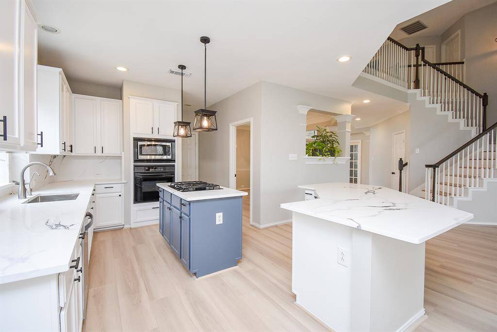 Bright, modern kitchen with white cabinetry, quartz countertops, and a central island. Features include a built-in oven, gas stove on the island, pendant lighting, and an open layout.