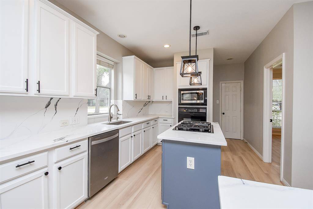 This kitchen features modern white cabinetry with sleek black handles, quartz countertops, and a central island with a gas cooktop, a built-in oven and microwave complement the bright and spacious design. Light flooring and pendant lighting add a warm touch.