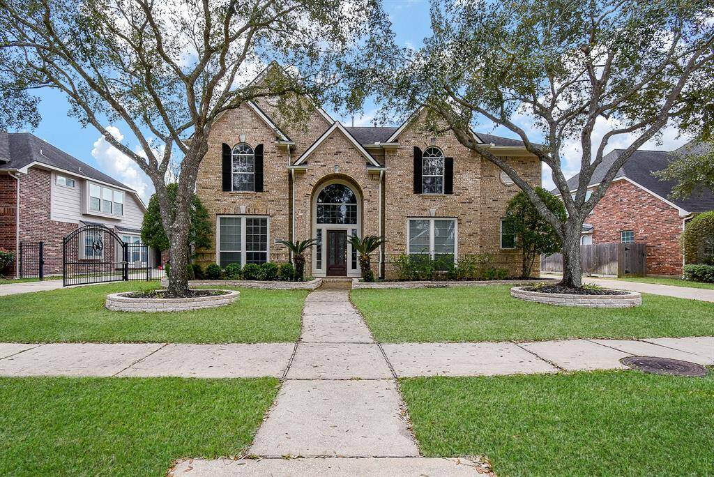 This is a charming two-story brick home with a symmetrical facade, featuring large arched windows and a welcoming central entrance. It's surrounded by well-maintained landscaping, including mature trees and lush green lawns, providing great curb appeal.