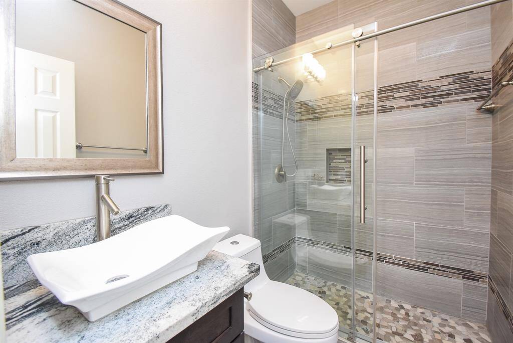 This modern second bathroom downstairs features a sleek glass-enclosed shower with stylish tile work, a contemporary vessel sink on a granite countertop, and a neutral color palette for a clean, sophisticated look.