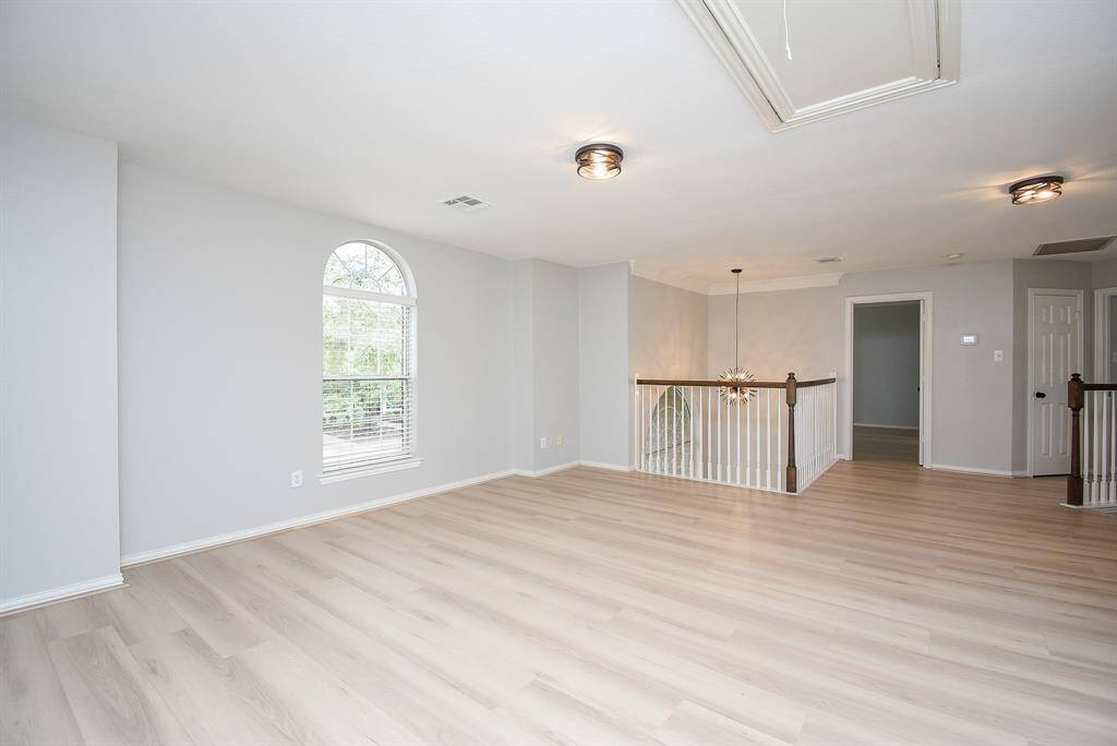 This game room is spacious and bright. It has a large arched window that allows natural light to filter in. The area includes a staircase with a stylish railing and a modern light fixture, offering an open and airy feel.