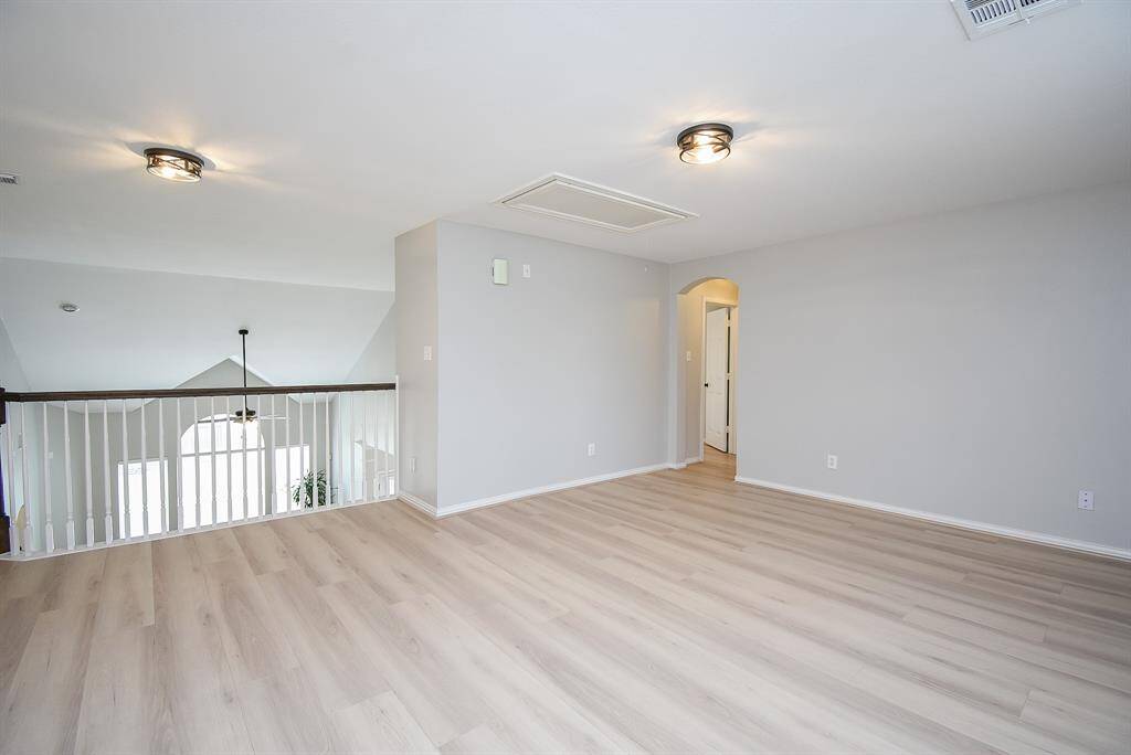 This photo shows game room overlooking the lower level through a railing. An arched doorway leads to the secondary bedroom.
