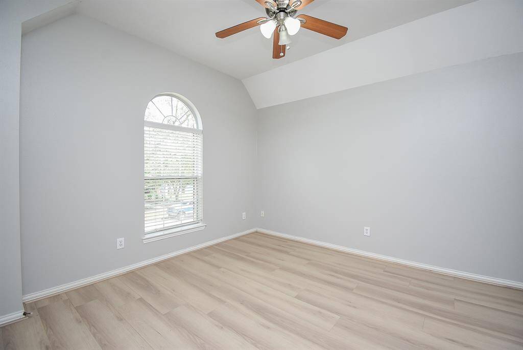 This bright room features a vaulted ceiling with a ceiling fan, and a large arched window, offering a spacious and airy feel.