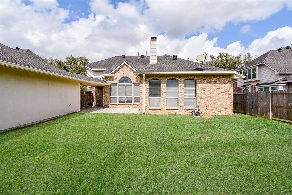 This photo showcases a spacious well-maintained backyard, a brick exterior of the house featuring large arched windows, and a fenced perimeter for privacy. The area is open and inviting, ideal for outdoor activities.