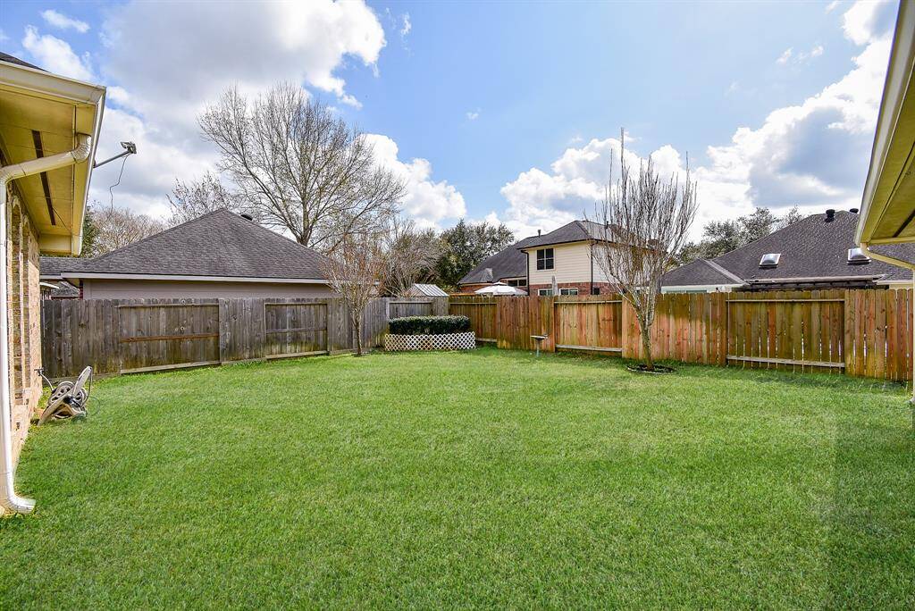 This photo shows a spacious, fenced backyard with lush green grass and a few trees. The area is surrounded by neighboring houses, providing a sense of community. Ideal for outdoor activities and relaxation.