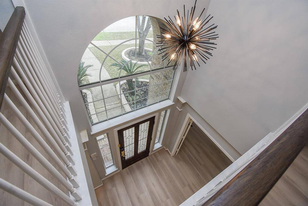 This photo showcases a bright, inviting entryway with a large window, modern chandelier, and great flooring. The space features a wooden staircase railing and a view of the exterior landscaping, creating an elegant first impression.