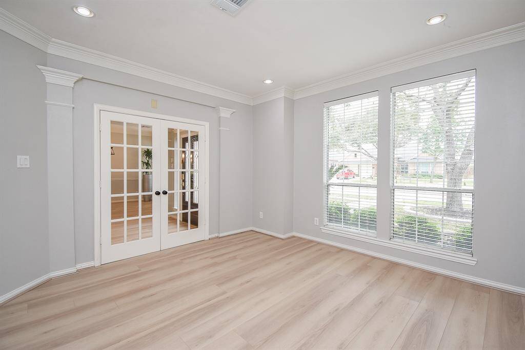 Bright and spacious room with large windows and elegant French doors. Features light LVP flooring, crown molding, and recessed lighting, creating a welcoming and airy atmosphere. Ideal for a home office or sitting room.