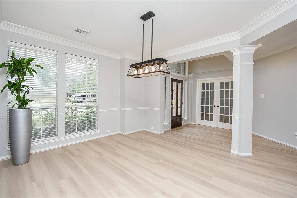 This bright, open dining room features elegant light flooring, large windows for natural light, and a modern chandelier. Perfect for a dining or living area.