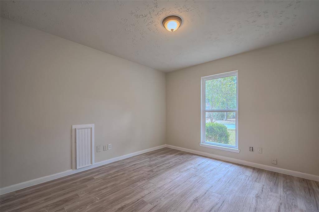 This is a bright secondary bedroom with neutral walls, textured ceiling, modern laminate flooring, and a large window offering natural light.