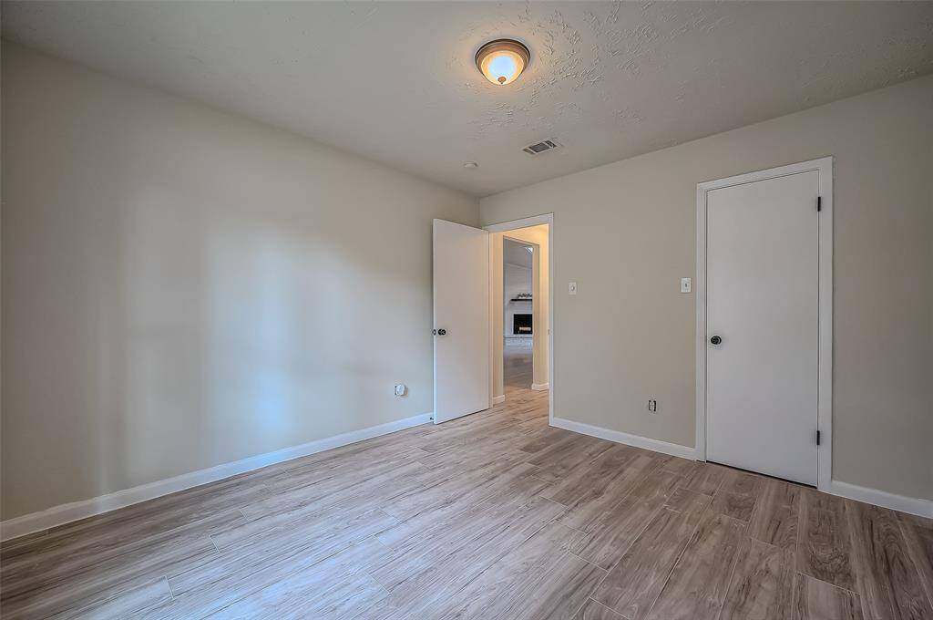 This spacious secondary bedroom features neutral walls, wood-look flooring and a ceiling light.