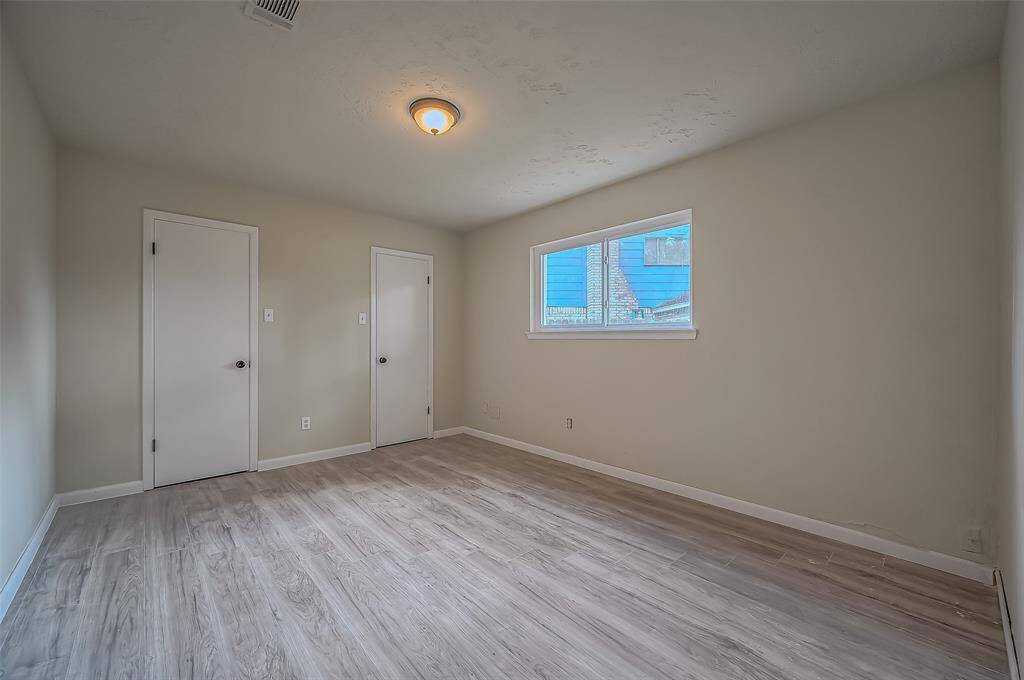 This is a bright, secondary bedroom with modern wood-look flooring, and a windows bringing in natural light.