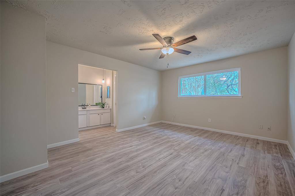 This is a bright, spacious primary bedroom with modern wood-look flooring, neutral wall colors, textured ceiling, and a ceiling fan.