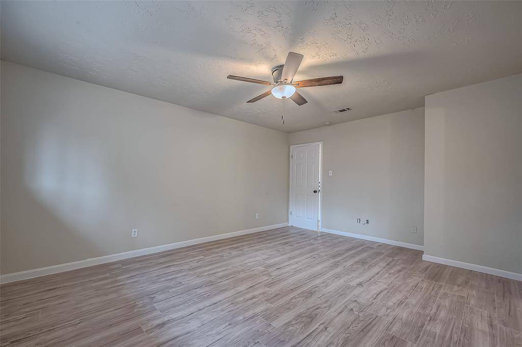 This is a spacious, well-lit room featuring contemporary wood-look flooring, neutral wall colors, and a textured ceiling with a modern ceiling fan.